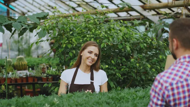 A smiling woman in an apron in a plant nursery Young smiling seller florist working in garden center. Woman gives shopping bag to customer at store indoors. Cultural, biological, and chemical pest controls compared for cut flower crops