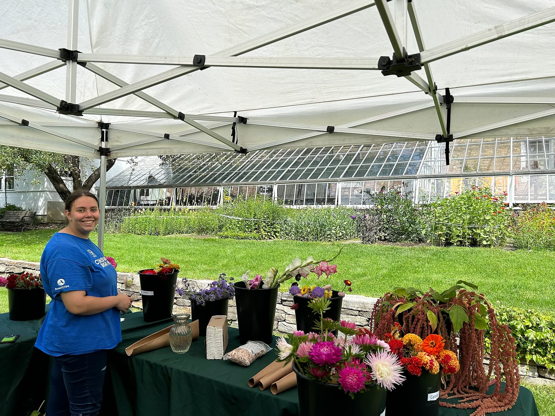 Park employee in blue shirt smiles at camera next to table with buckets of cut flowers Intern Avery displays bouquet making options. 9 honest notes on postharvest loss turnaround