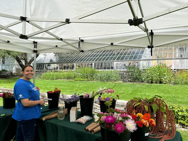 Park employee in blue shirt smiles at camera next to table with buckets of cut flowers Intern Avery displays bouquet making options. 9 honest notes on postharvest loss turnaround